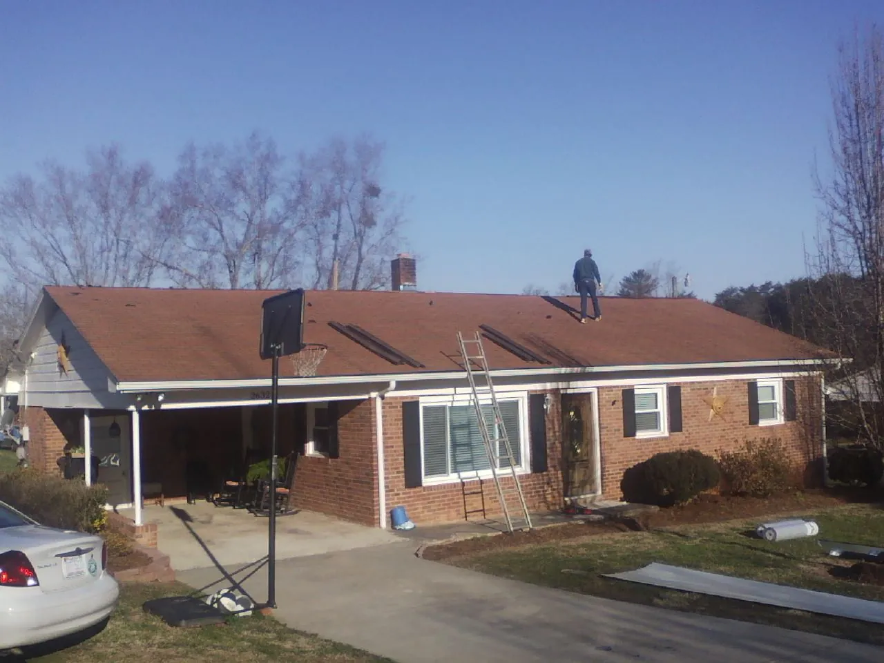 Roofer stripping a shingle roof on a brick ranch before metal panels in Dallas